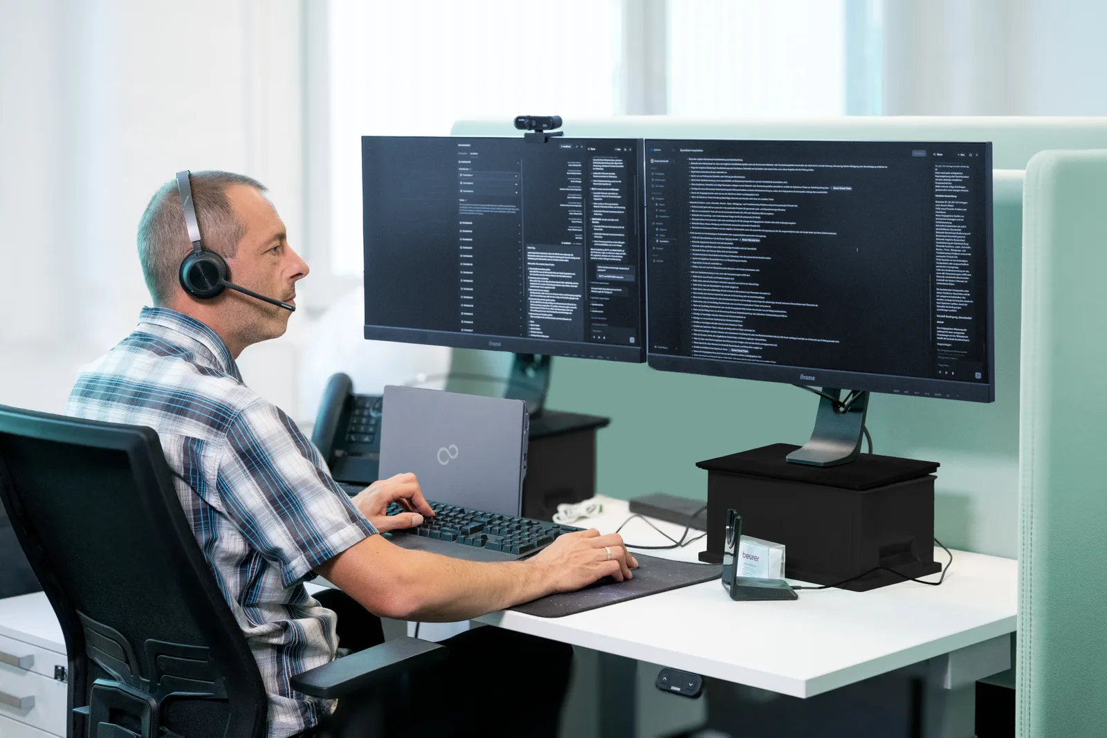 Daniel Braun handling a request at his desk with a headset and two screens